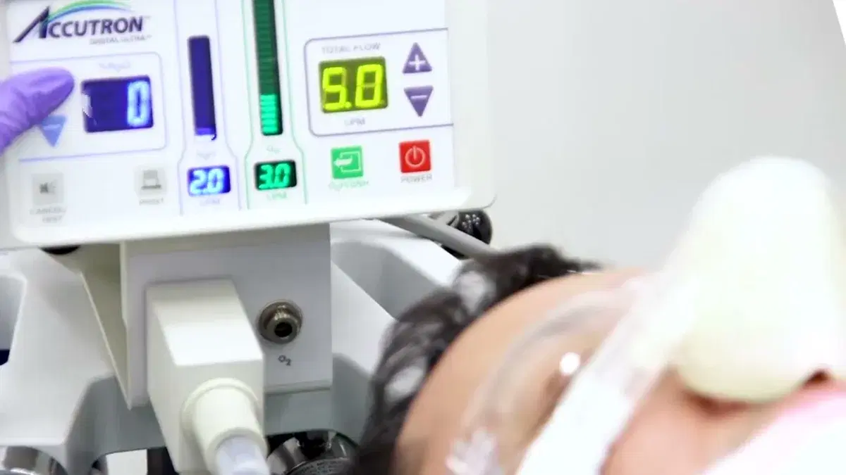 Paciente adulto recostado con la mascarilla nasal puesta; delante, el flujómetro Accutron marcando la mezcla y la mano enguantada del dentista