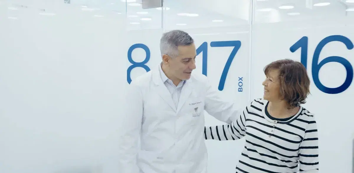 Pasillo de la clínica con las puertas de los box numeradas, un odontólogo acompañando a una paciente