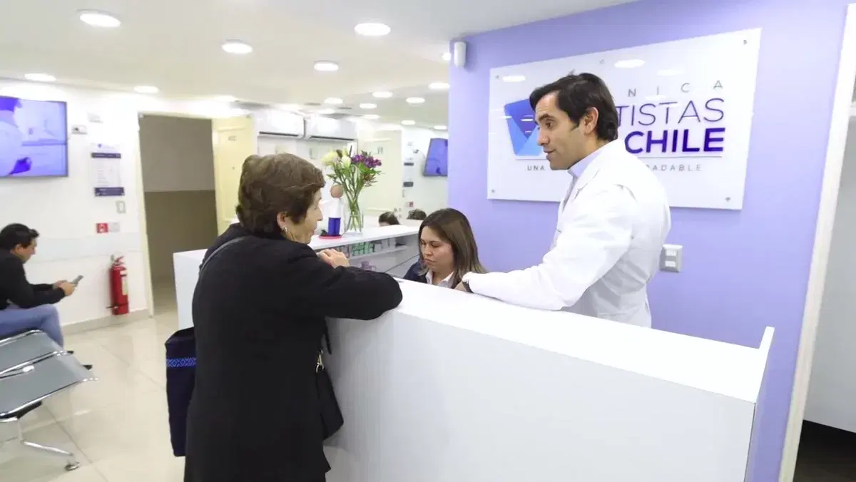 Mesón de recepción de la clínica en Providencia: un odontólogo atiende a una paciente y al fondo se ve la sala de espera