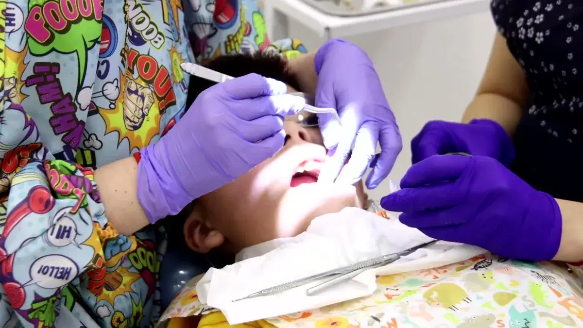 Niño recostado en el sillón con lentes de protección mientras la odontopediatra le limpia los dientes con espejo bucal e instrumento