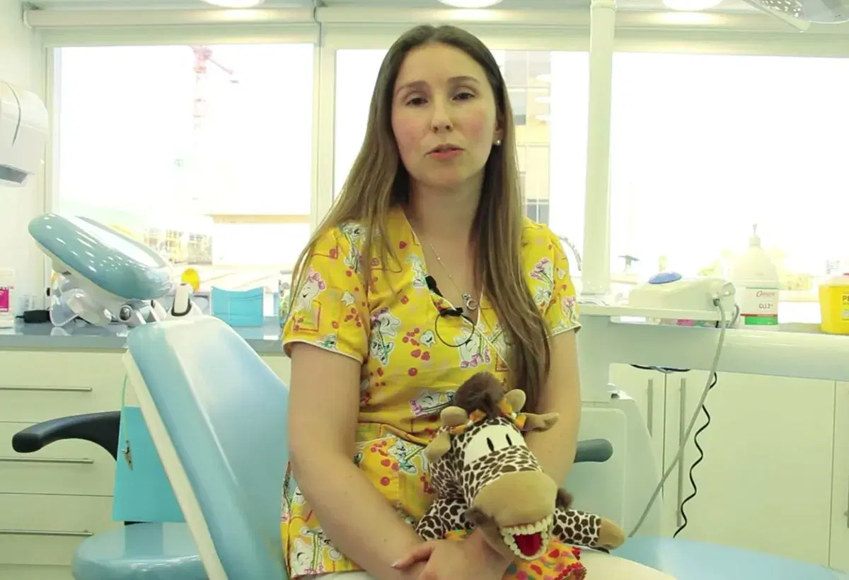 Odontopediatra sentada en el box infantil con un títere de jirafa en las manos, junto al sillón dental