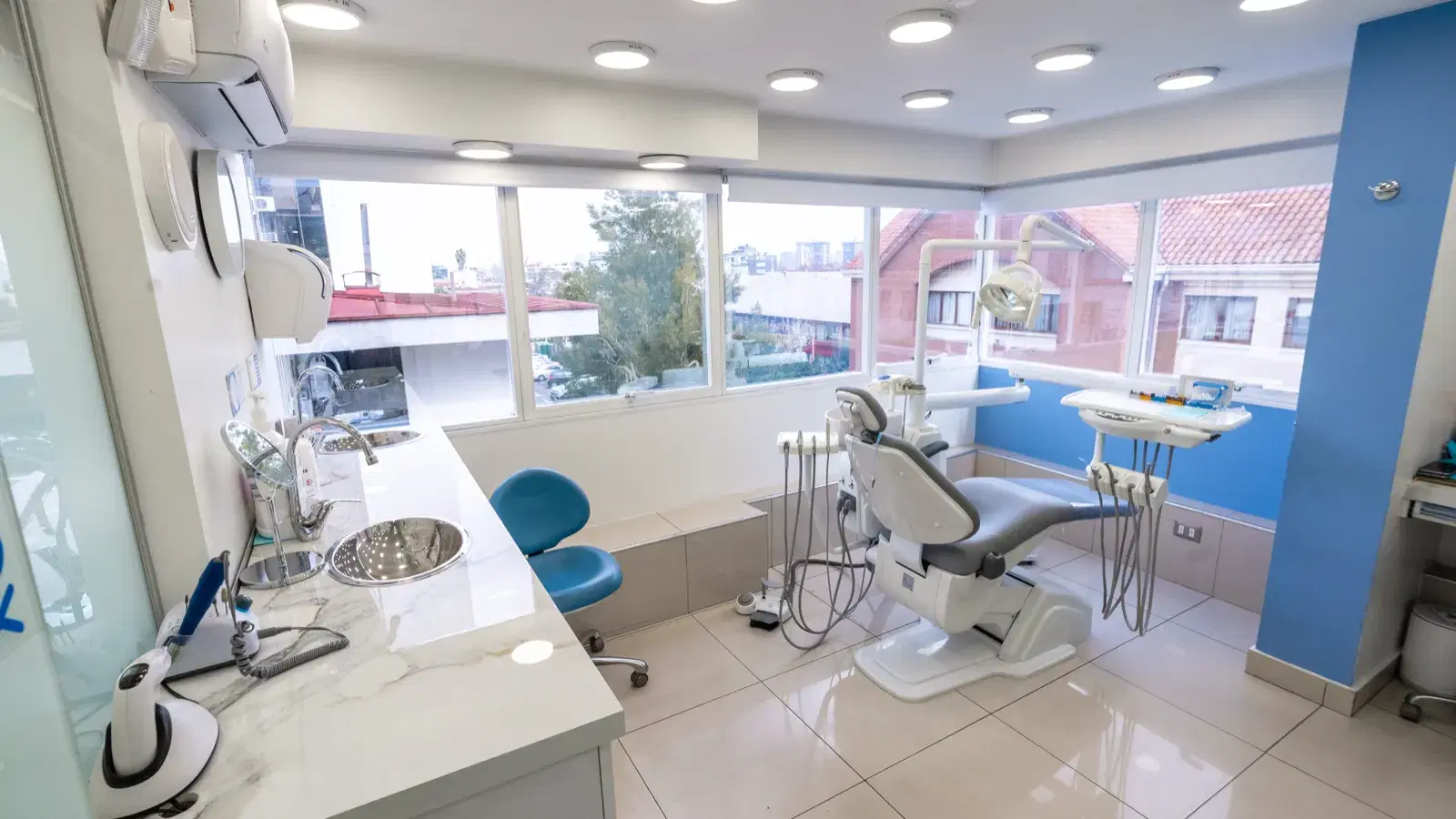 Box clínico con sillón dental, lámpara y mueble de trabajo, iluminado por ventanales