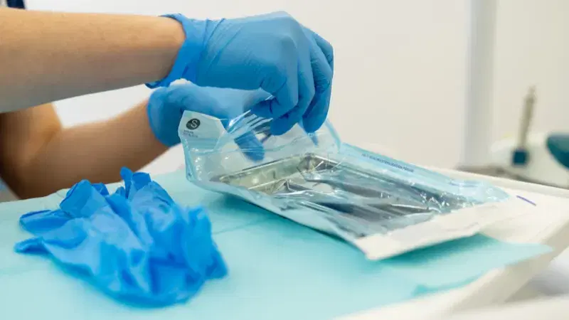 Manos con guantes manipulando instrumental esterilizado dentro de su bolsa sellada
